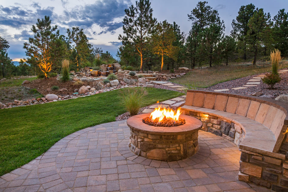 a gorgeous rock and landscaping at the back of a villa, concrete stamped flooring with concrete elevated firepit, concrete chair at the side